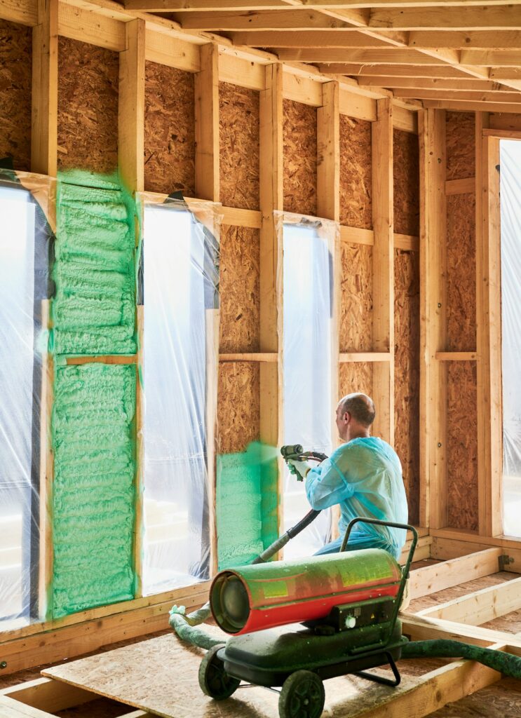 Worker spraying polyurethane foam for insulating wooden frame house.